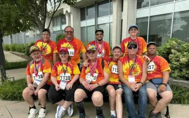 Special Olympics athletes and coaches posing together in tie-dye team shirts with medals