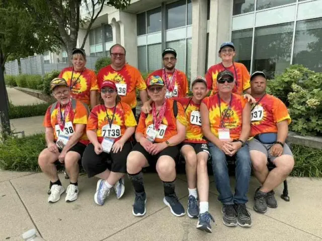 Special Olympics athletes and coaches posing together in tie-dye team shirts with medals
