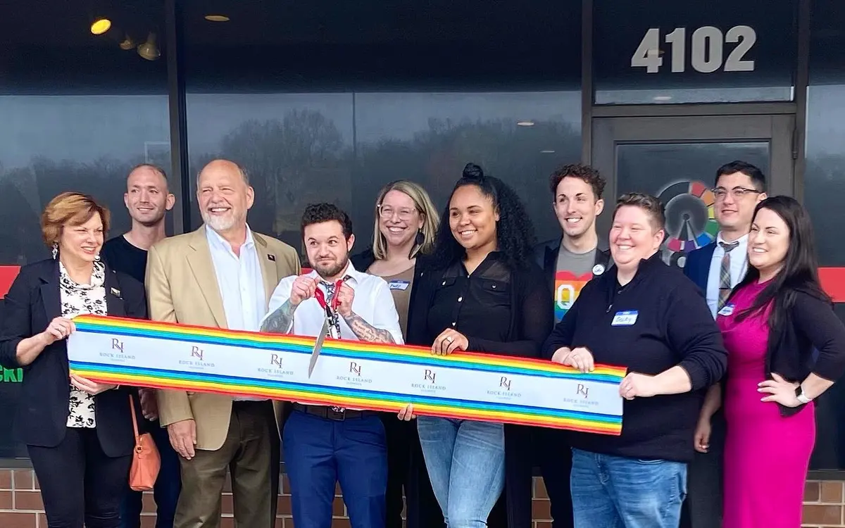Staff, leadership, and local supporters holding a ceremonial rainbow ribbon outside the Clock, Inc. community center