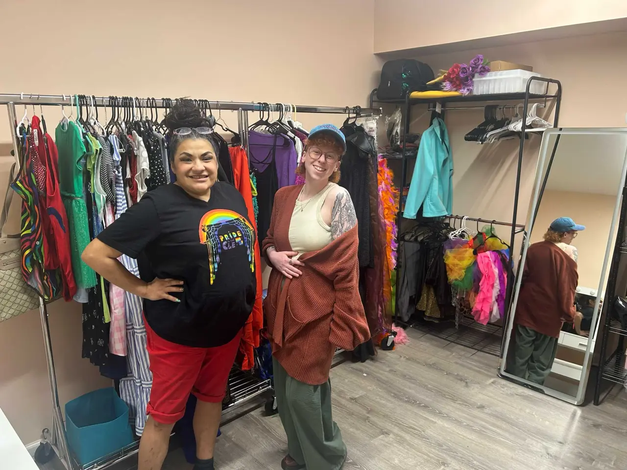 Two smiling center staff members standing by clothing racks inside the Pride Expression affirming clothing closet