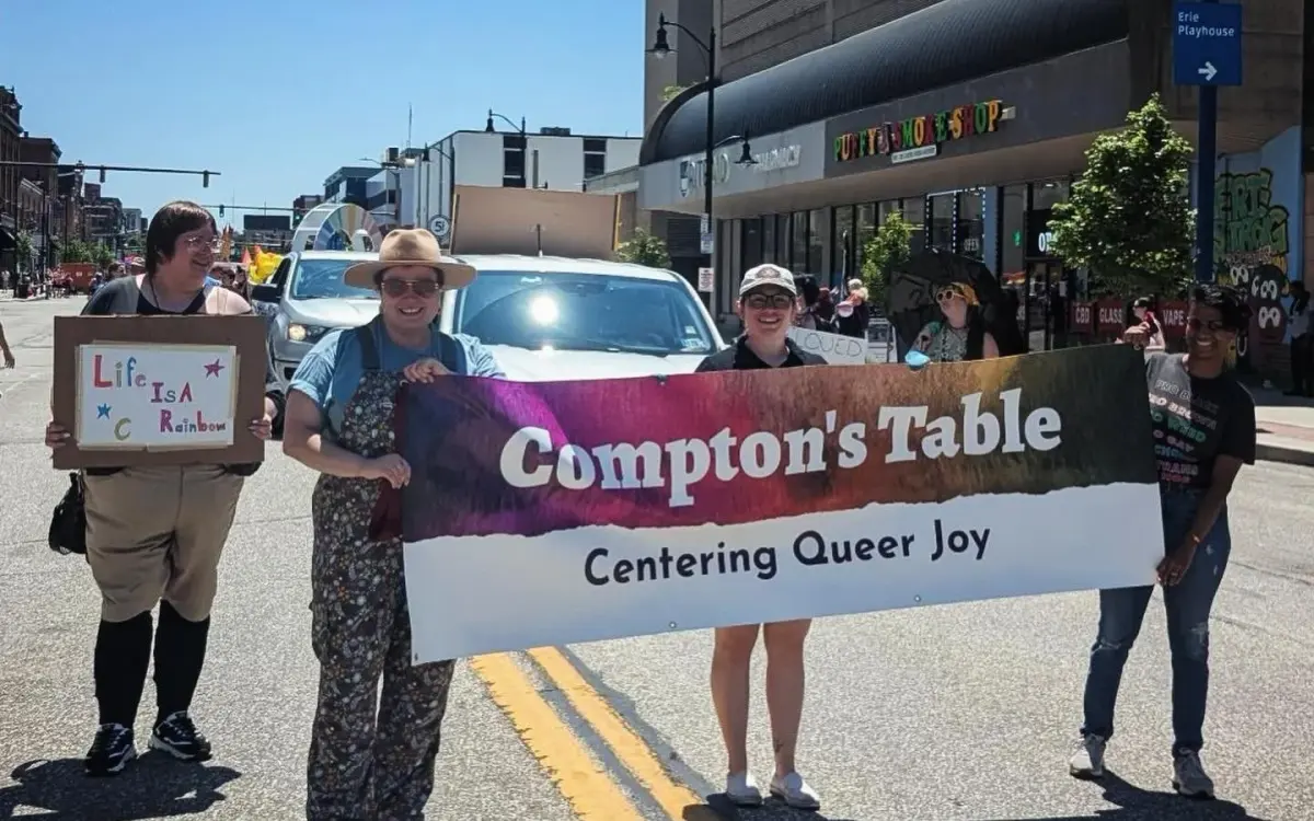 Compton's Table community members marching in a Pride parade holding a banner that reads Compton's Table Centering Queer Joy