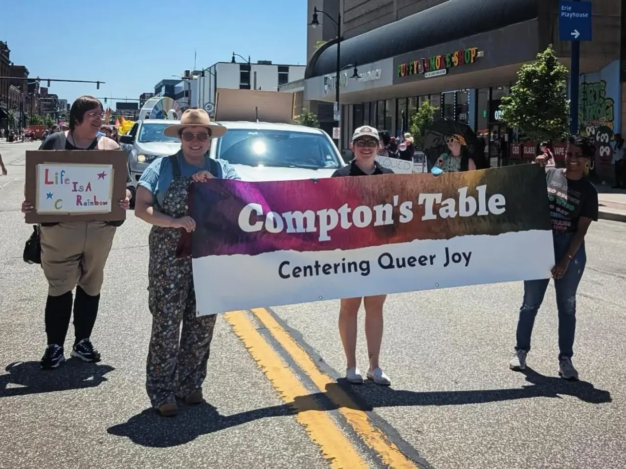 Compton's Table community members marching in a Pride parade holding a banner that reads Compton's Table Centering Queer Joy