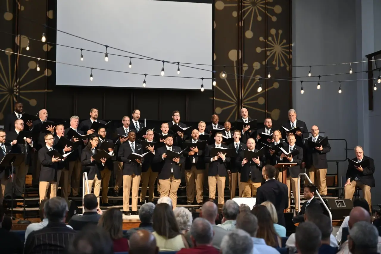 The Gay Men's Chorus of Tampa Bay singing on stage in black jackets before an audience