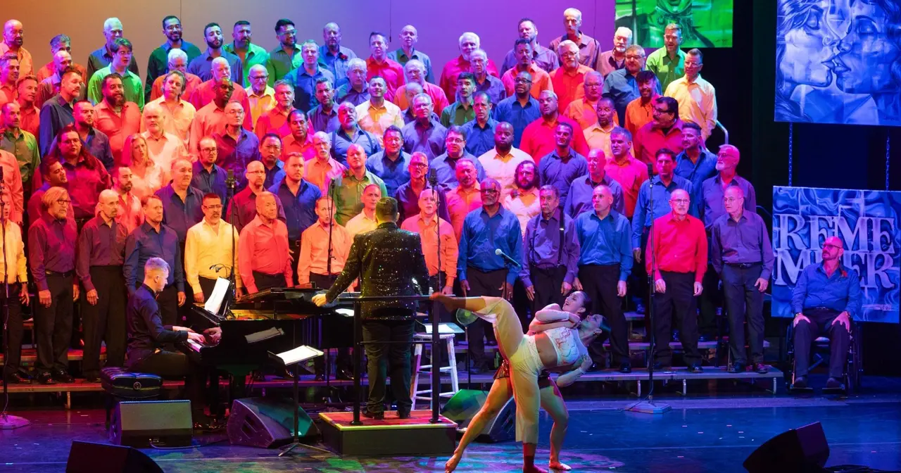 The Gay Men's Chorus of South Florida in rainbow-colored shirts performing on stage with a dancer
