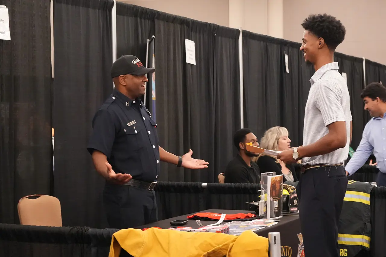 A firefighter recruiter talking with a young job seeker at a GSUL job fair