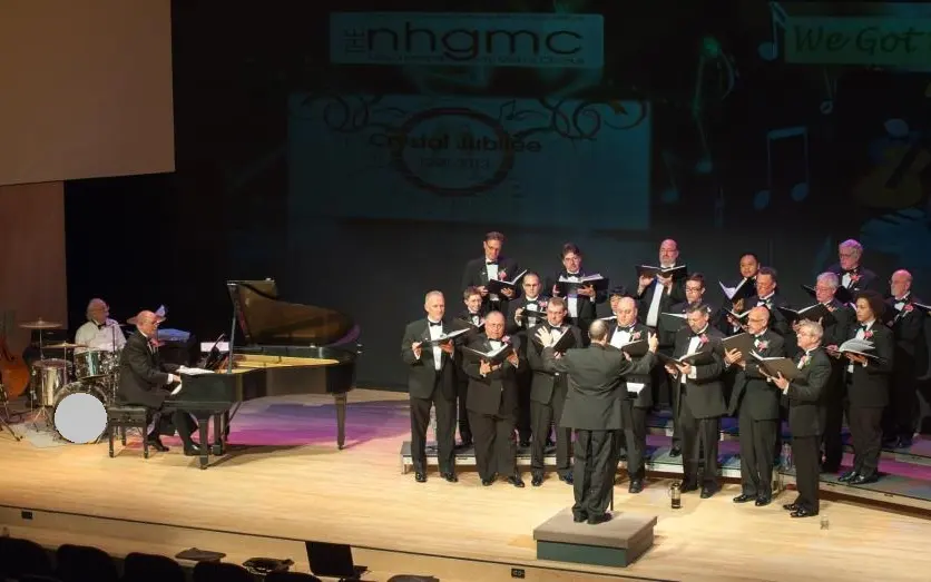 New Hampshire Gay Men's Chorus performing on stage with their conductor and accompanist