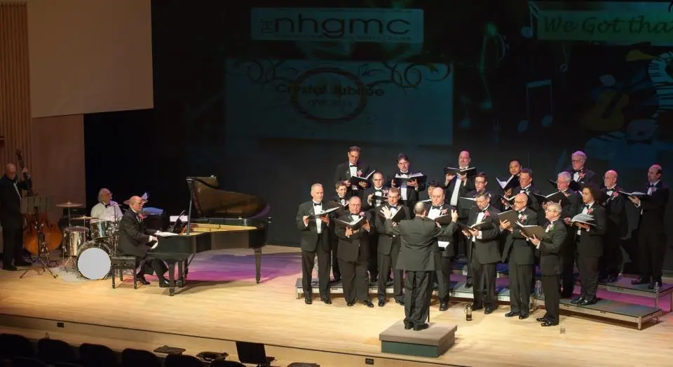 New Hampshire Gay Men's Chorus performing on stage with their conductor and accompanist