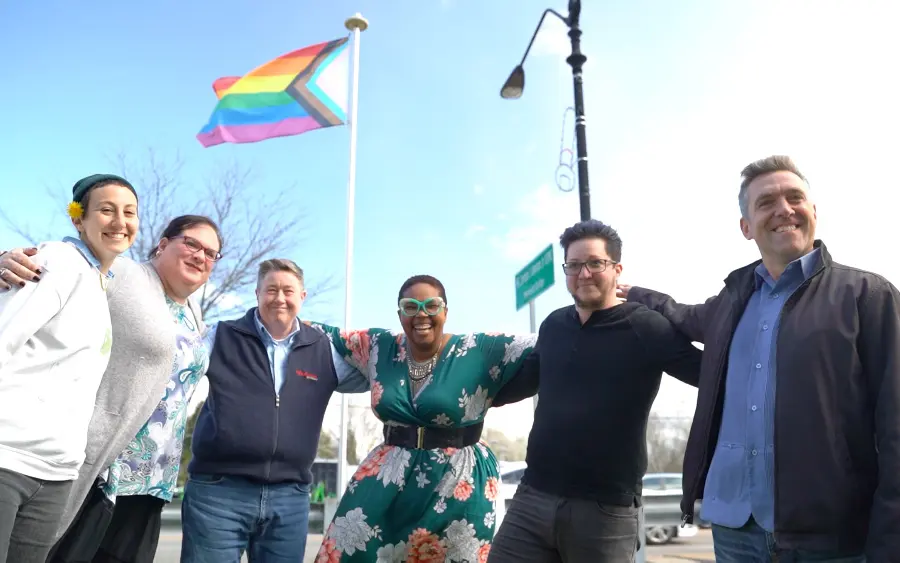SAGA Community Center staff and volunteers holding the Progress Pride flag outdoors