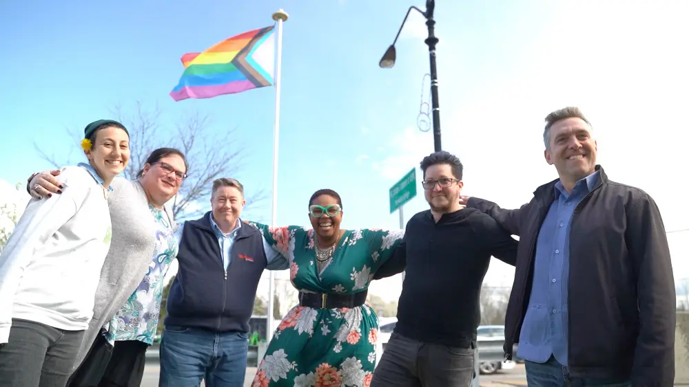 SAGA Community Center staff and volunteers holding the Progress Pride flag outdoors
