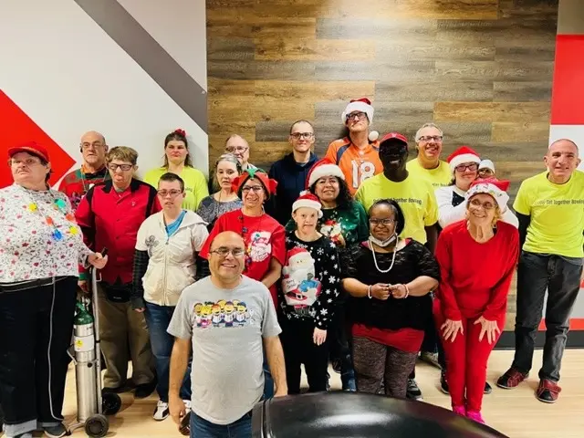A group of Arc of Aurora members in holiday outfits smiling together at a bowling alley