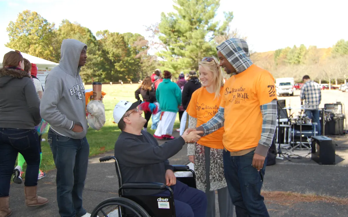 A participant in a wheelchair shaking hands with an Arc Walk volunteer at a community event