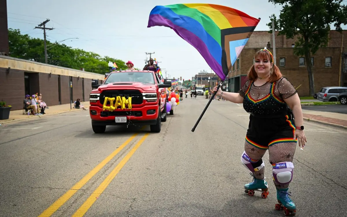 A roller skater holding the Progress Pride flag leading the Liam Foundation truck in the Pride parade