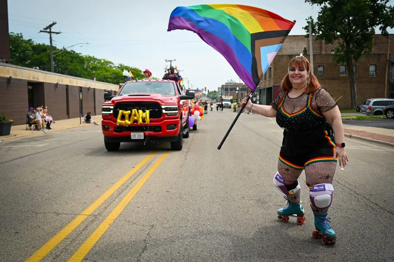 A roller skater holding the Progress Pride flag leading the Liam Foundation truck in the Pride parade