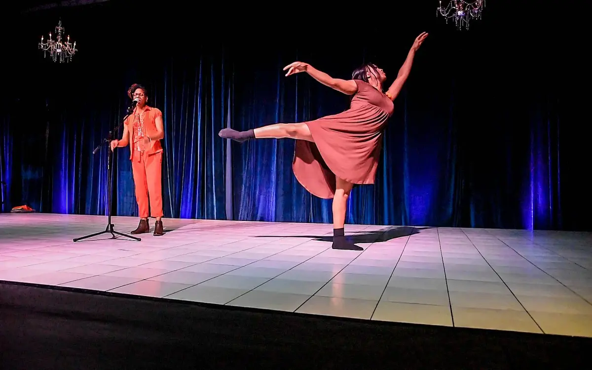 Dancers and vocalists performing on a lighted stage during an installment