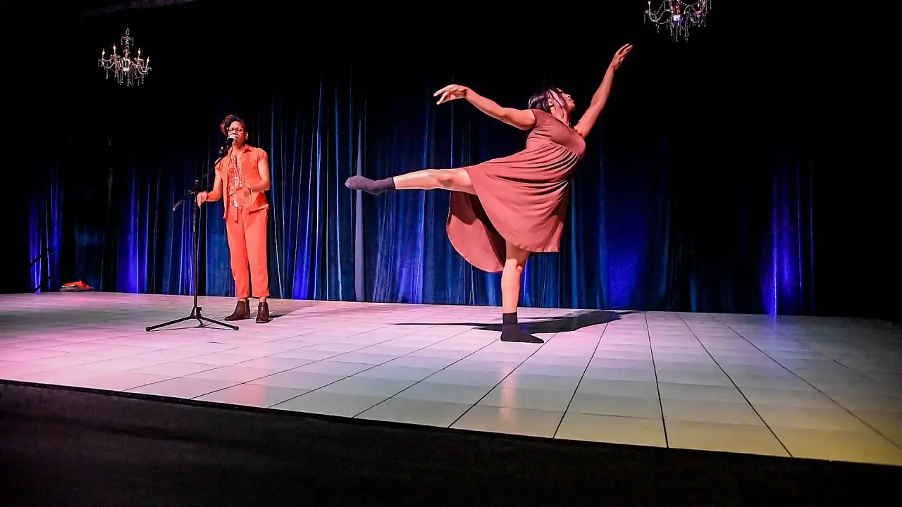 Dancers and vocalists performing on a lighted stage during an installment