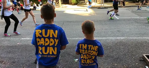 Two young boys in UPS for Downs marathon shirts watching runners along the race route