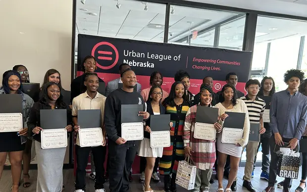 Students and graduates proudly holding certificates in front of the Urban League of Nebraska banner