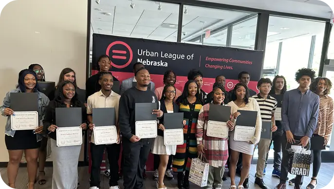 Students and graduates proudly holding certificates in front of the Urban League of Nebraska banner