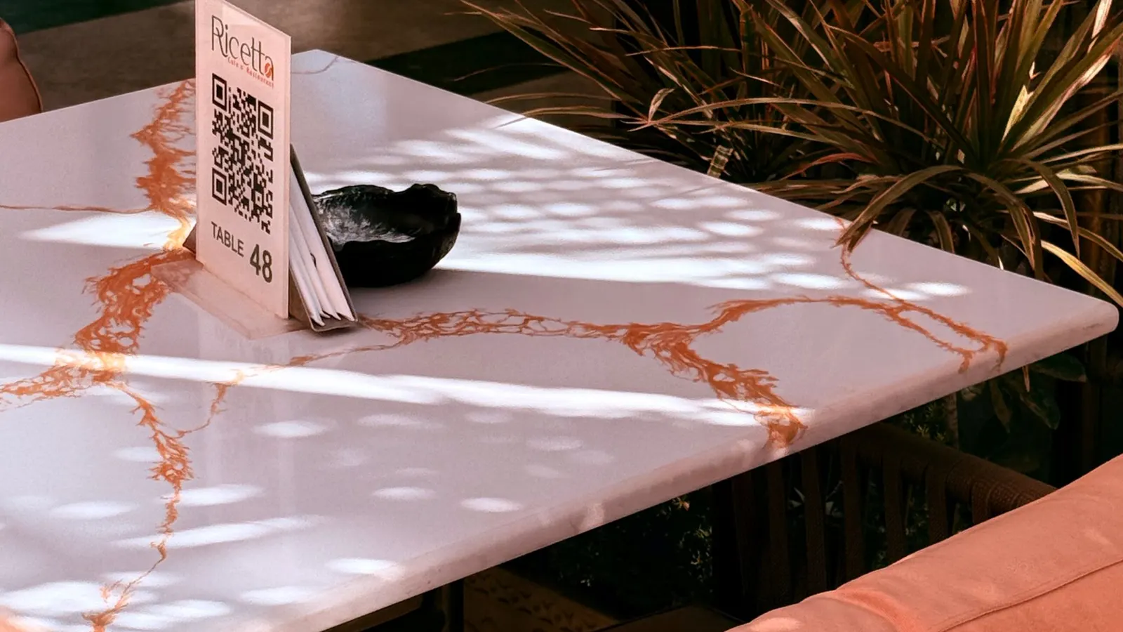 A marble cafe table with a small tent card showing a QR code and a table number, in dappled sunlight