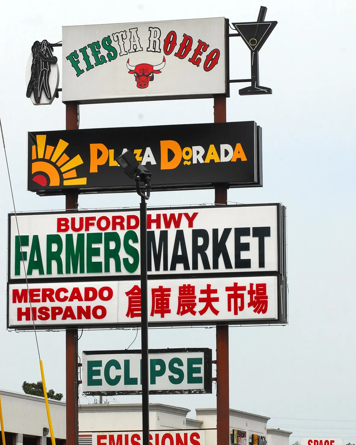 A tall shopping center sign on Buford Highway in metro Atlanta reading Plaza Dorada and Buford Hwy Farmers Market, with Mercado Hispano in Spanish and the market's name in Chinese characters