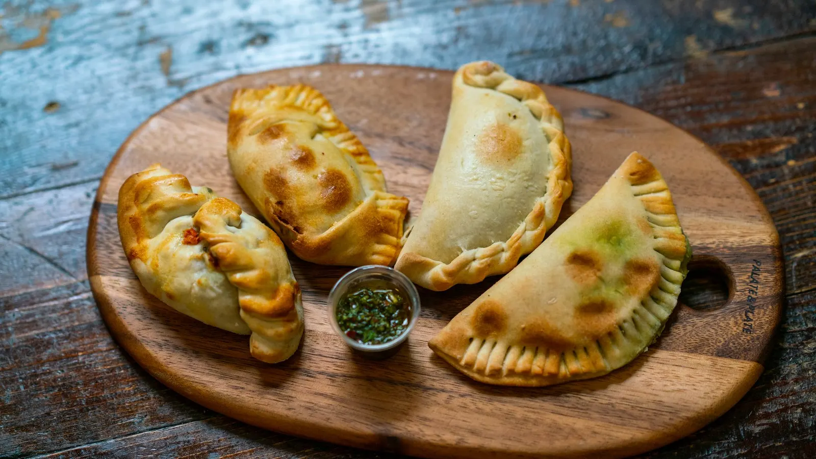 Golden baked empanadas on a wooden board with a small bowl of green sauce