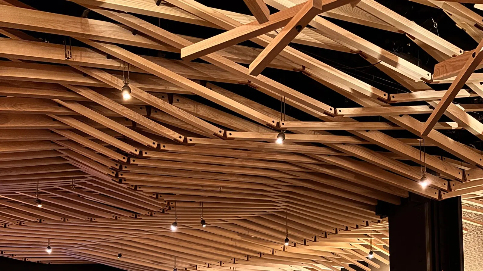 A restaurant ceiling covered in a flowing pattern of wooden slats with small lights set between them